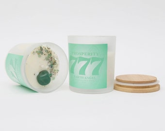 May include: Two frosted glass candle jars with green lids. The candle on the left has a green stone and green glitter inside. The candle on the right has the text "PROSPERITY 777 EARTHANGEL" printed on the front. A wooden lid is also shown.