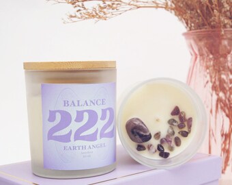 May include: A purple and white candle with a wooden lid. The candle is labelled "BALANCE 222 EARTHANGEL Amethyst 10 oz". The candle is sitting on a purple box with a small glass jar filled with amethyst crystals.