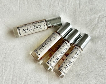 May include: Five silver roller bottles containing clear liquid and dried flowers. Each bottle has a white label with black text that reads "EARTH ANGEL APHRODITE GODDESS OF LOVE, BEAUTY, PASSION 10 ML."