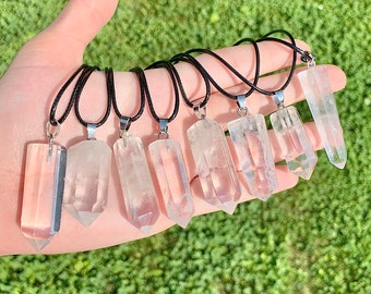 May include: A set of eight clear quartz crystal point pendants on black cords. The pendants are all different sizes and shapes, but they are all clear and have a pointed tip.