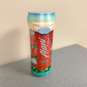 May include: A cylindrical Alani Nu energy drink can featuring a red background with white text and strawberry graphics. The can is topped with a light blue and white plastic lid. The design includes small white flowers near the base and orange slices.