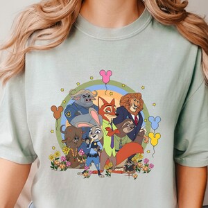 A woman wearing a t-shirt with a graphic of various cartoon characters, including a police officer, a fox, and other animals, along with flowers and balloons. She is holding a white mug in her hand.