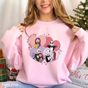 A woman wearing a pink sweatshirt with a graphic of characters from the movie " jack Skellington and Sally".