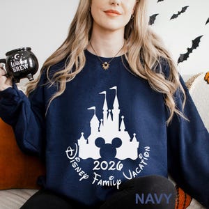 A woman wearing a navy blue sweatshirt with a white castle and Mickey Mouse design, holding a black mug with the text "Disney BREW" on it.