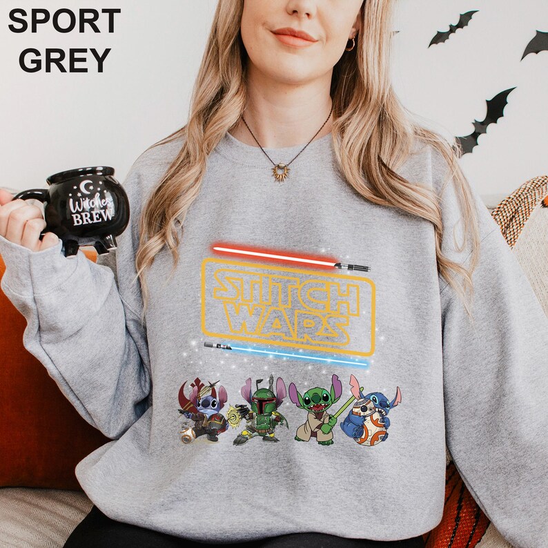 A woman wearing a grey sweatshirt with a Star Wars logo and characters printed on it, holding a black mug with the Star Wars logo.