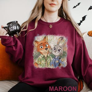 A woman wearing a maroon sweater with a graphic of two cartoon characters, a fox and a rabbit, on it.