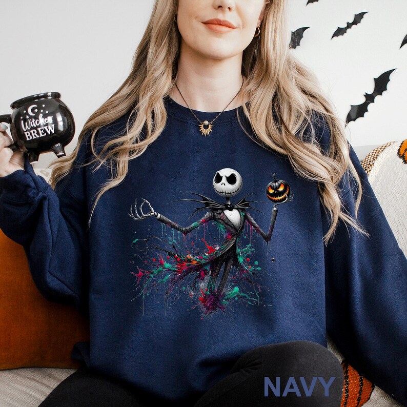 A woman wearing a navy blue sweatshirt with a graphic of a jack-o-lantern and a skeleton figure, holding a black mug with a "Witch Brew" design.