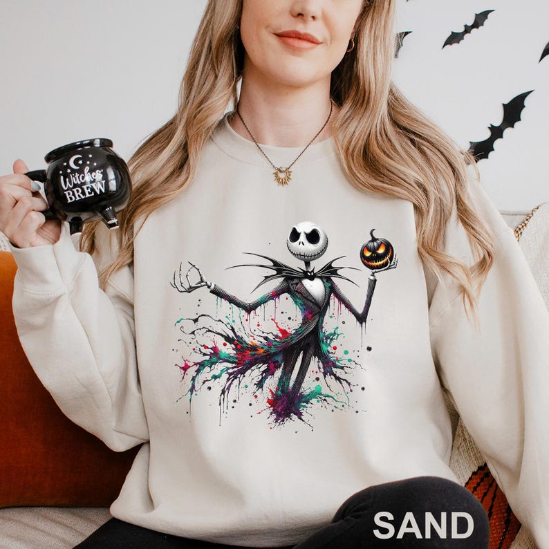 A woman wearing a white sweatshirt with a graphic of a jack-o-lantern and a mug with the text "Witch's Brew" printed on it.