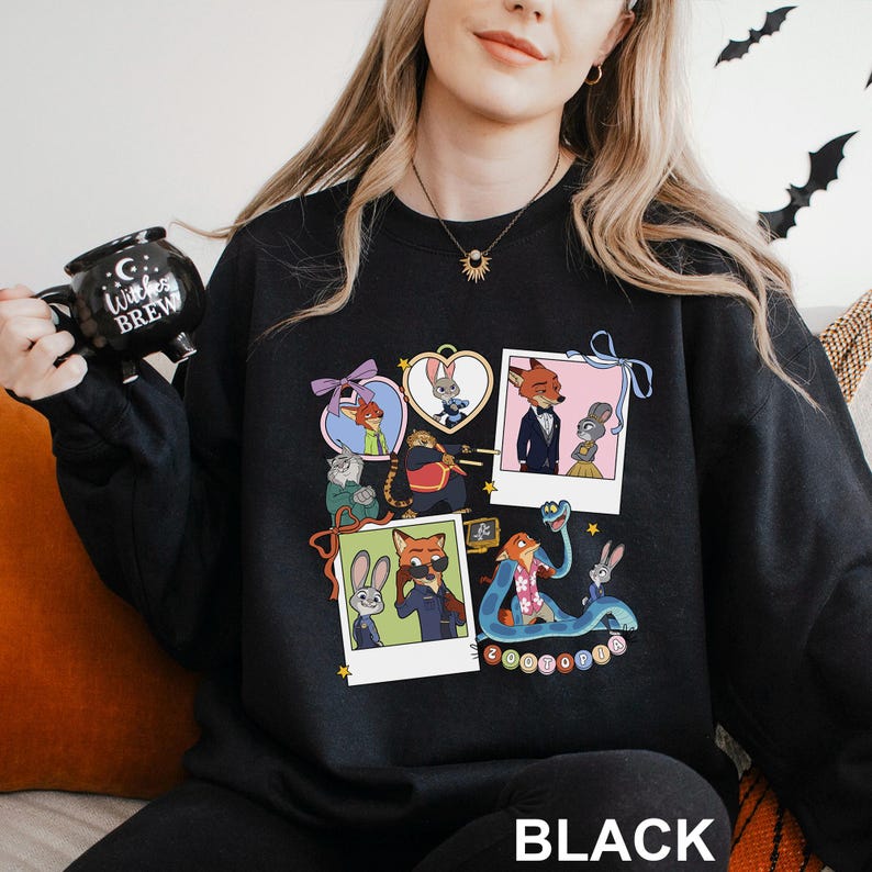 A woman wearing a black sweatshirt with a colorful graphic of cartoon characters on it, holding a black mug with the text "Witch Brew" printed on it.