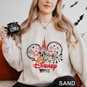 A woman wearing a white sweater with a Disney-themed design, holding a mug with the text "Witch's Brew" on it.