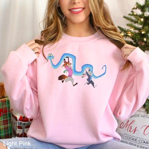 A woman wearing a pink sweatshirt with a cartoon character on it, smiling and posing with her hair in front of a Christmas tree.