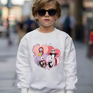 A young boy wearing a white sweatshirt with a graphic of characters from the movie " Nightmare Before Christmas" and sunglasses.