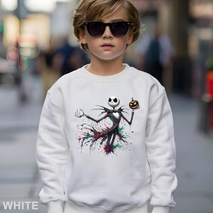 A young boy wearing a white sweatshirt with a graphic of a jack-o-lantern character printed on it.