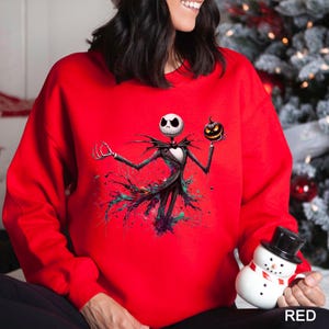 A woman wearing a red sweater with a Jack Skellington character from the movie "The Nightmare Before Christmas" printed on it. She is holding a small snowman figure.