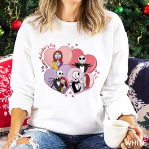 A woman wearing a white sweater with a graphic design featuring characters from the movie " Nightmare Before Christmas".