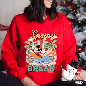 A woman wearing a red sweater with a cartoon character and the text "Spring Break" printed on it, holding a snowman.