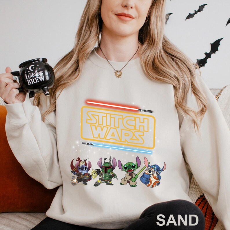 A woman wearing a white sweatshirt with a Star Wars logo and characters printed on it, holding a mug with a Star Wars-themed design.