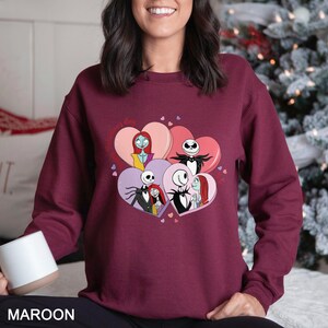 A woman wearing a burgundy sweatshirt with a graphic of characters from the movie " Nightmare Before Christmas" and hearts around them.