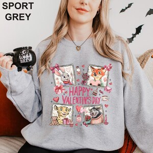 A woman wearing a grey sweatshirt with a graphic design featuring cartoon animal characters and the text "Happy Valentine's Day".