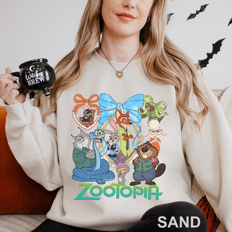 A woman wearing a white sweatshirt with a cartoon character design and holding a mug with a witch brew logo.