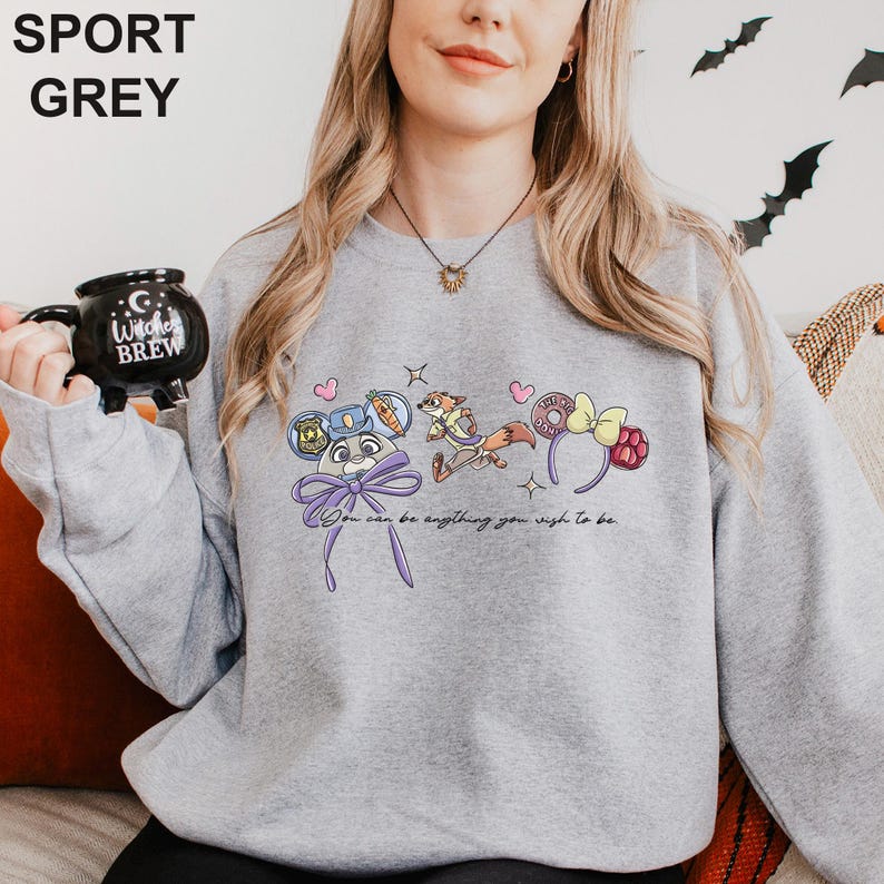 A woman wearing a grey sweatshirt with a cartoon character design and text printed on it, holding a black mug.