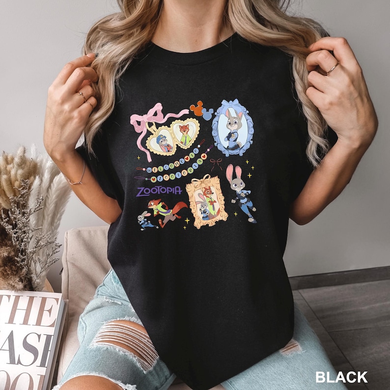 A woman wearing a black t-shirt with a colorful graphic design featuring cartoon characters and text.