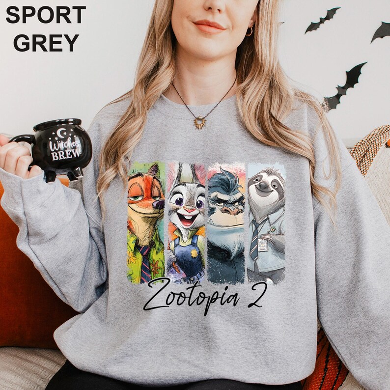 A woman wearing a grey sweatshirt with a graphic of four cartoon animal characters from the movie "Zootopia 2" printed on it. She is holding a black mug with the text "Zootopia Brew" printed on it.
