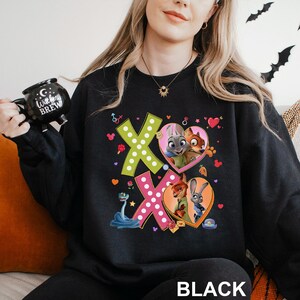 A woman wearing a black sweatshirt with a colorful graphic design featuring cartoon characters and the text 'XOXO'.