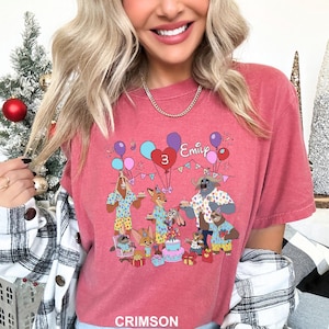 A woman wearing a pink t-shirt with a cartoon image of a birthday party featuring a dog, a cat, and other animals.