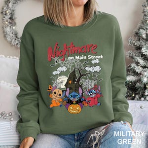 A woman wearing a green sweatshirt with a Halloween-themed graphic design featuring characters from the movie "Nightmare on Main Street".
