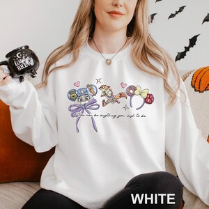 A woman wearing a white sweatshirt with a graphic design of cartoon characters and text.