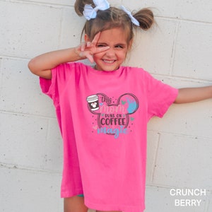 a little girl wearing a pink t - shirt with a cup of coffee on it