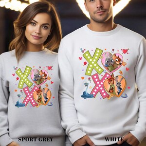 Two people wearing matching white sweatshirts with colorful cartoon characters and hearts printed on them.