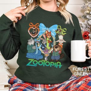 A woman wearing a green sweatshirt with a colorful graphic of cartoon animals, including a cat, rabbit, and dog, along with the word "Zootopia". She is holding a white mug in her hand.