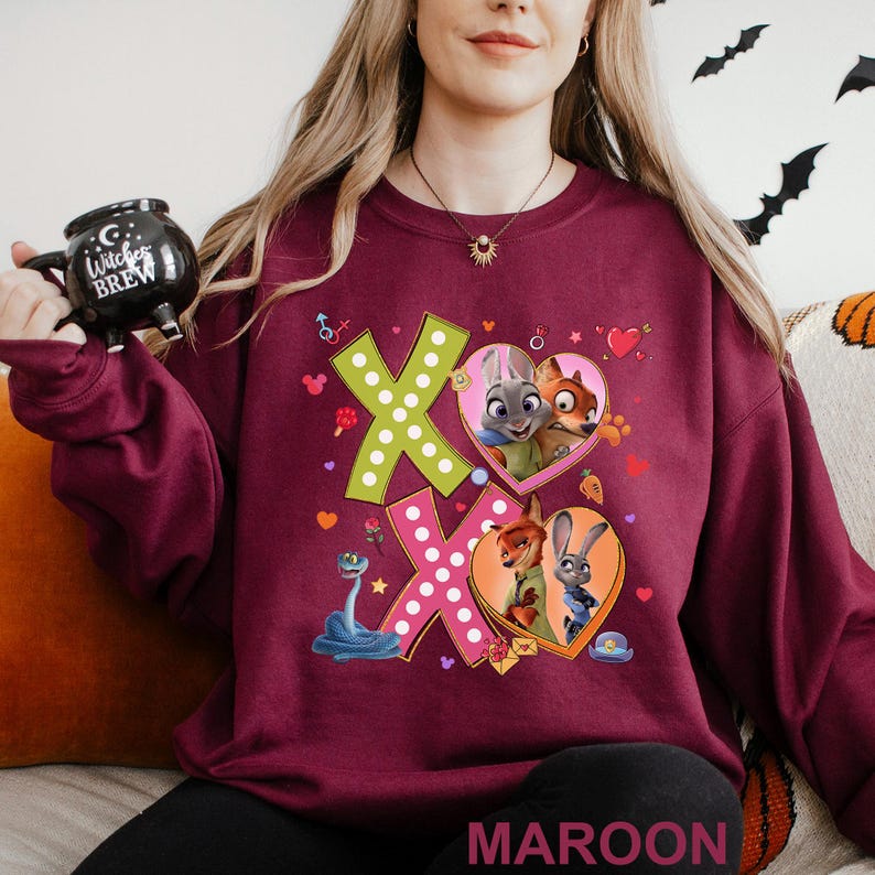 A woman wearing a maroon sweater with a graphic design featuring cartoon characters and a large "X" on the front.