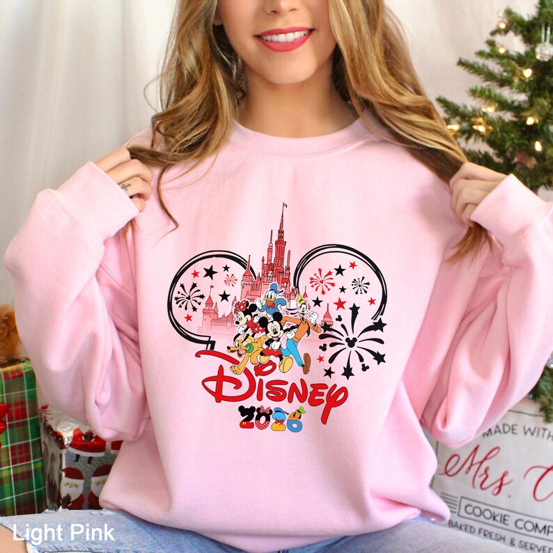 A woman wearing a pink sweatshirt with a Disney logo and fireworks design.