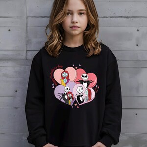 A young girl wearing a black sweatshirt with a graphic design featuring characters from the movie " jack Skellington".