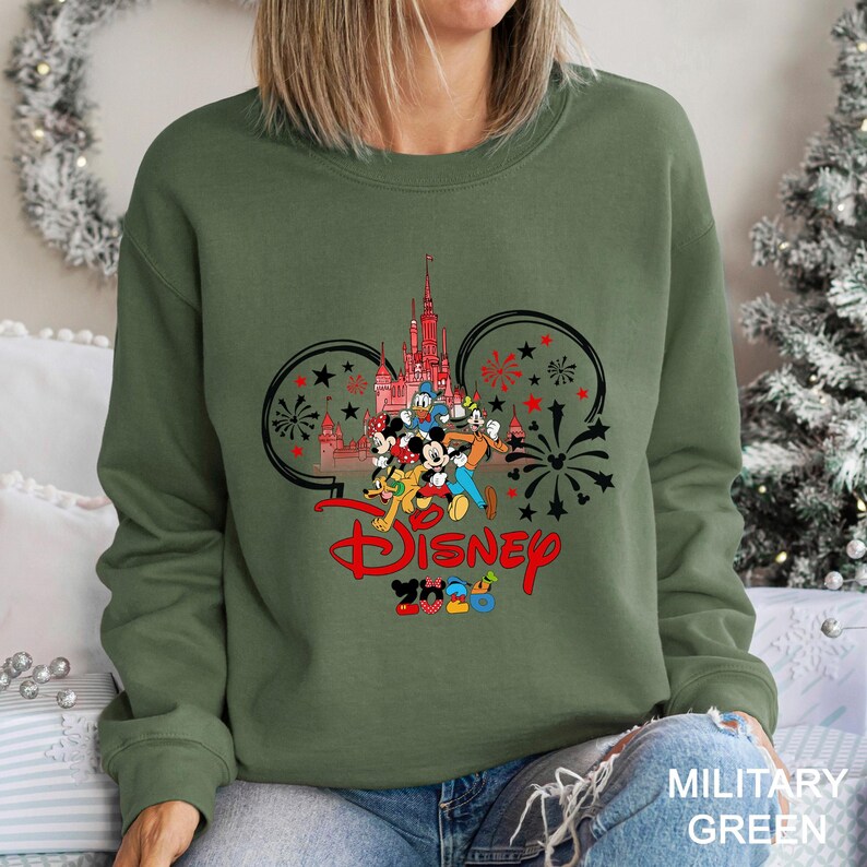 A woman wearing a green sweatshirt with a Disney-themed graphic design featuring Mickey Mouse and other Disney characters.
