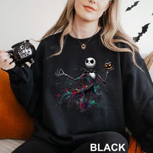 A woman wearing a black sweatshirt with a graphic of a jack-o-lantern and a mug with the text "Cocktails" printed on it.