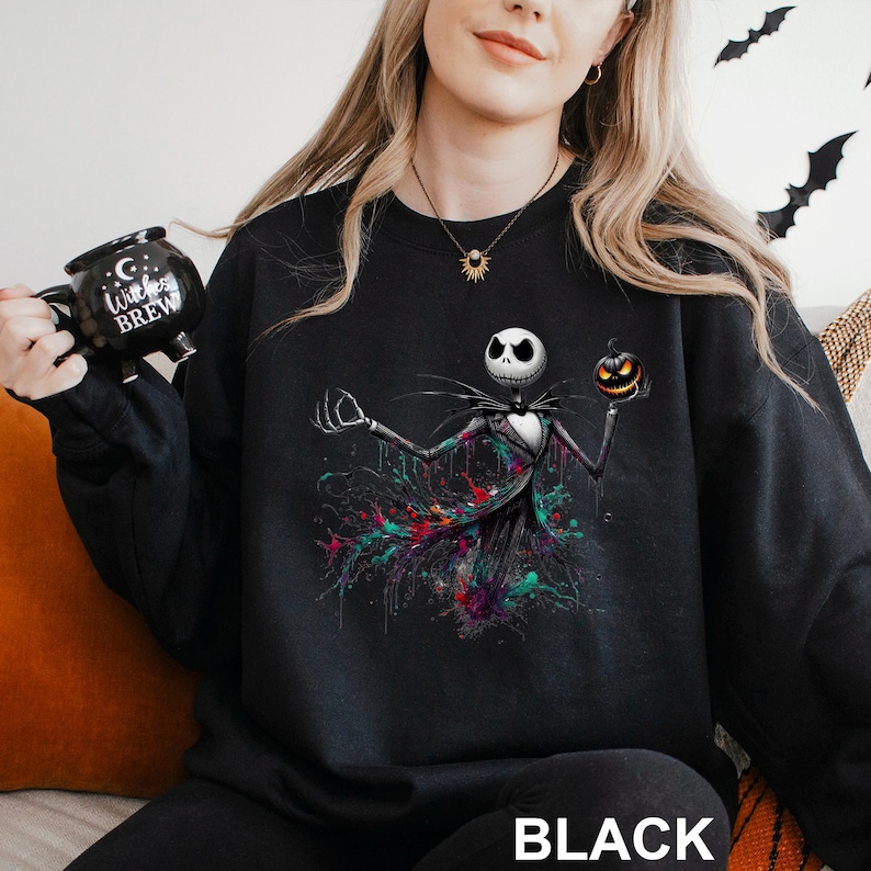 A woman wearing a black sweatshirt with a graphic of a jack-o-lantern and a mug with the text "Cocktails" printed on it.