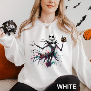 A woman wearing a white sweatshirt with a graphic of a jack-o-lantern character printed on it.