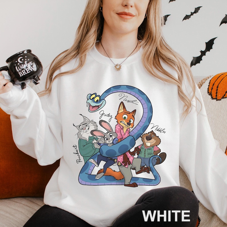 A woman wearing a white sweatshirt with a cartoon character design, including a snake, rabbit, and other animals. She is holding a mug with a black design featuring a moon and stars.