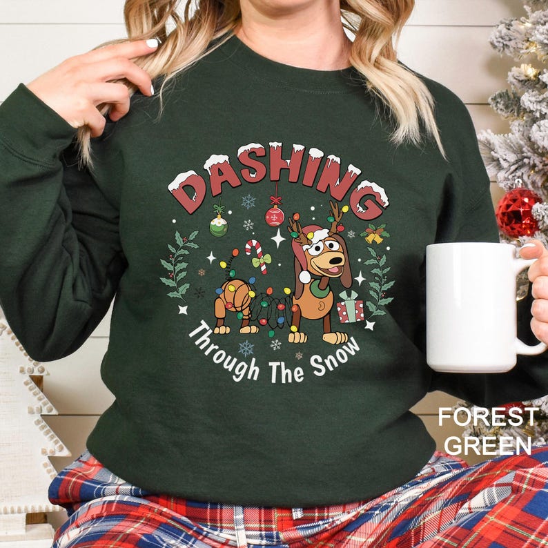 A woman wearing a green sweater with a Christmas-themed design, including a cartoon dog and snowflakes, holding a white mug.