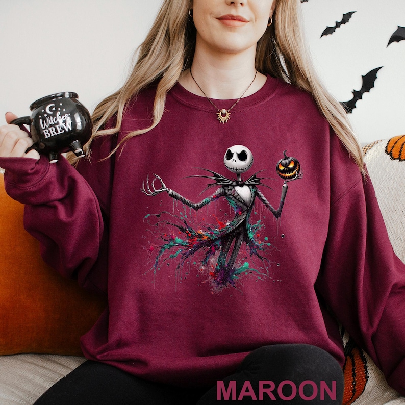 A woman wearing a maroon sweater with a graphic of a jack-o-lantern and a mug with the text "C witch brew" printed on it.