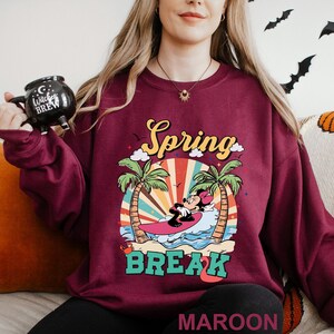 A woman wearing a maroon sweater with a graphic design of Minnie Mouse riding a surfboard and the text "Spring BREAK" printed on it.