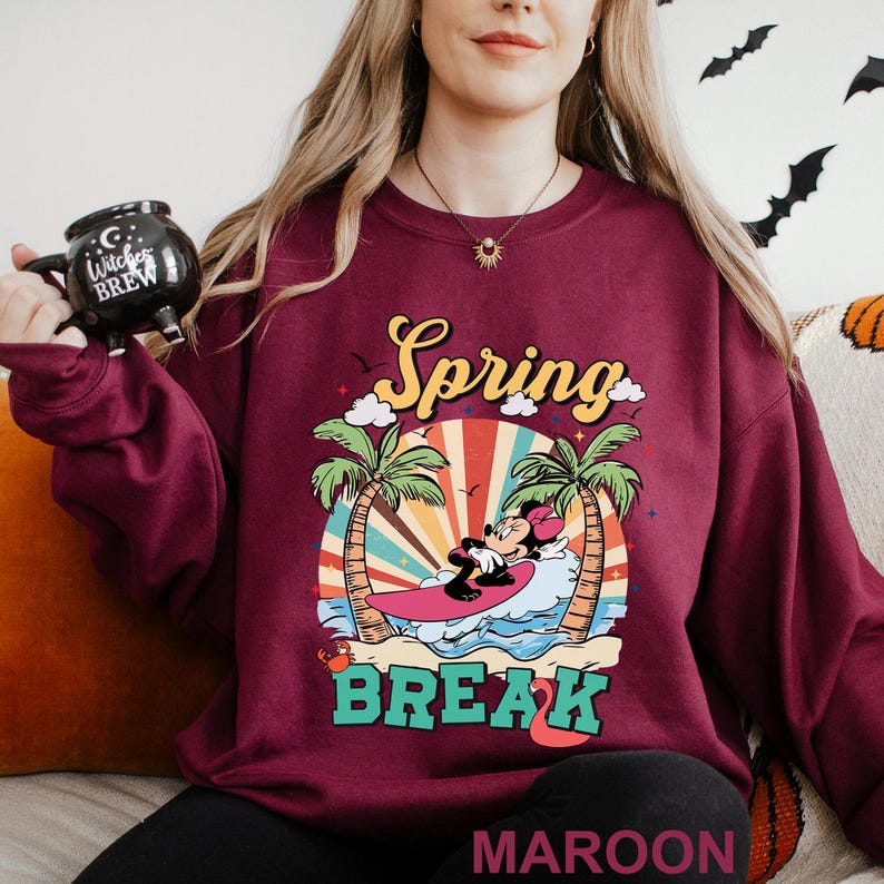 A woman wearing a maroon sweater with a graphic design of Minnie Mouse riding a surfboard and the text "Spring BREAK" printed on it.