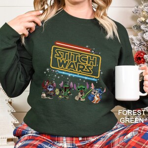 A woman wearing a green sweatshirt with a Star Wars logo and characters printed on it, holding a white mug.
