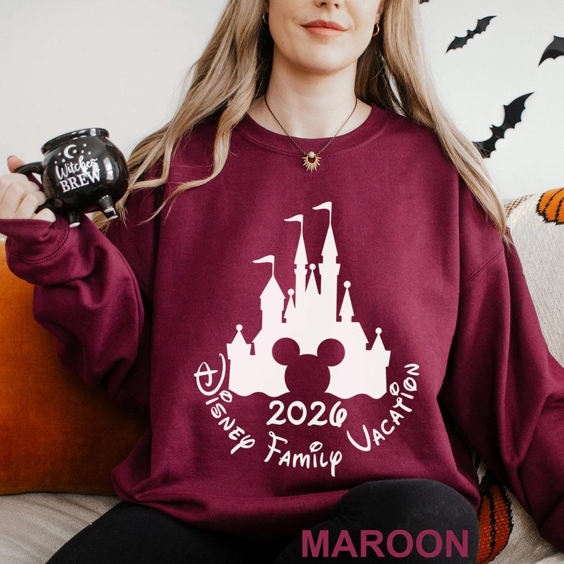 A woman wearing a maroon sweater with a white castle and Mickey Mouse design, holding a black mug with the text "Disney Family Vacation" printed on it.