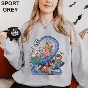 A woman wearing a grey sweatshirt with a cartoon character design, holding a black mug with the text "Coffee Brew" on it.
