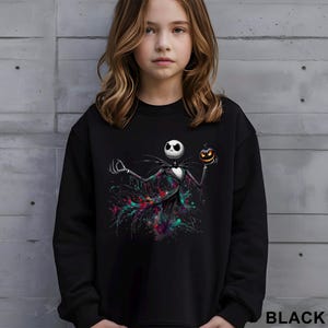 A young girl wearing a black sweatshirt with a graphic of a jack-o-lantern character on it.